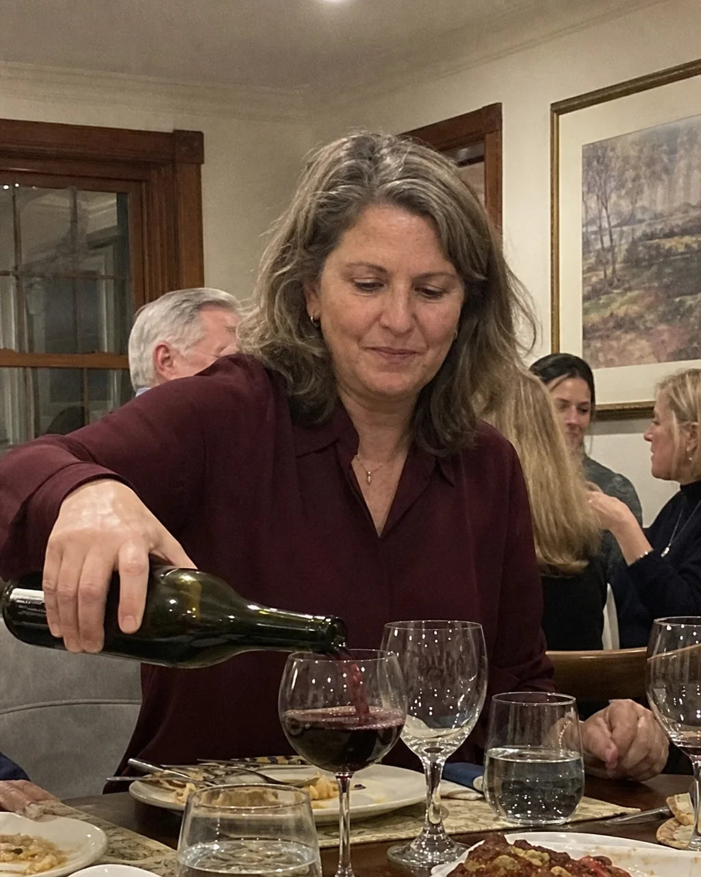 Woman quietly topping up her wine glass at a dinner table