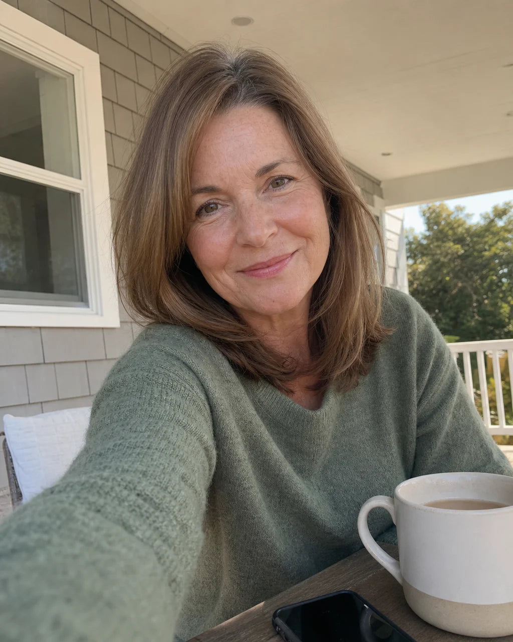 Woman smiling warmly on her porch holding a mug
