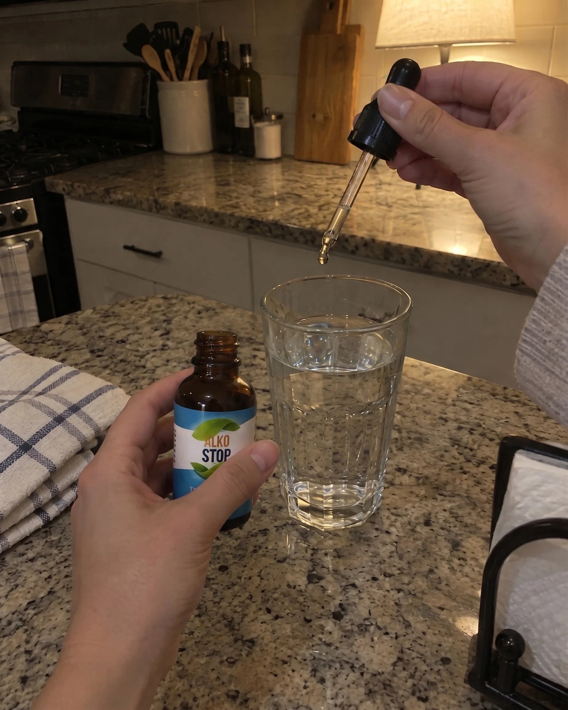 Hand holding AlkoStop dropper bottle over a glass of water
