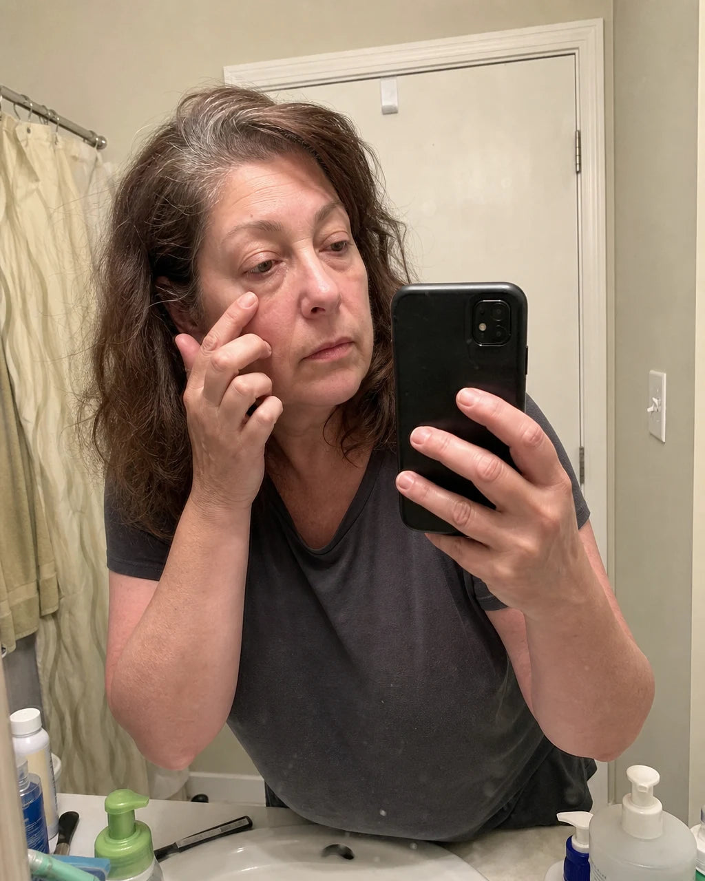 Woman examining tired eyes in the bathroom mirror